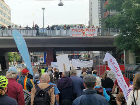 Demonstrationståget passerar under en bro på Sveavägen. På bron finns fler demonstranter med en banderoll.